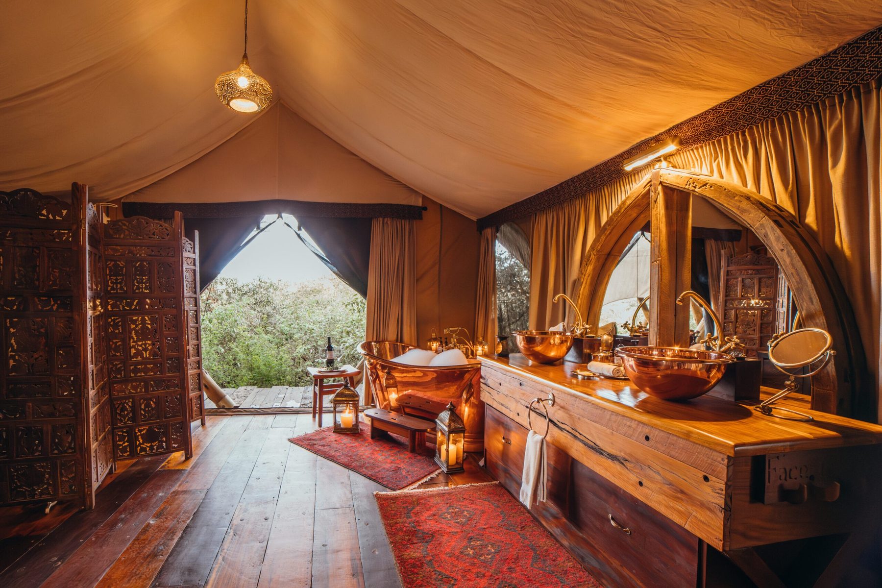 Lamplit tent interior at Mara Nyika Camp with rugs on wooden floors, a long vanity and doors open to the bush