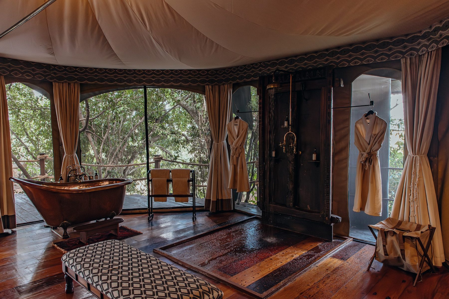 Bathroom at Mara Plains Camp with a copper bathtub, a wooden wardrobe and tall windows onto the trees