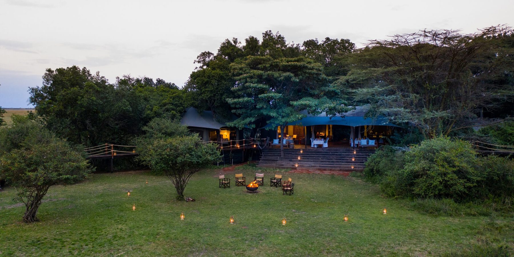 Lantern-lit lawn in front of the canvas tents of Mara Plains Camp, surrounded by trees at dusk