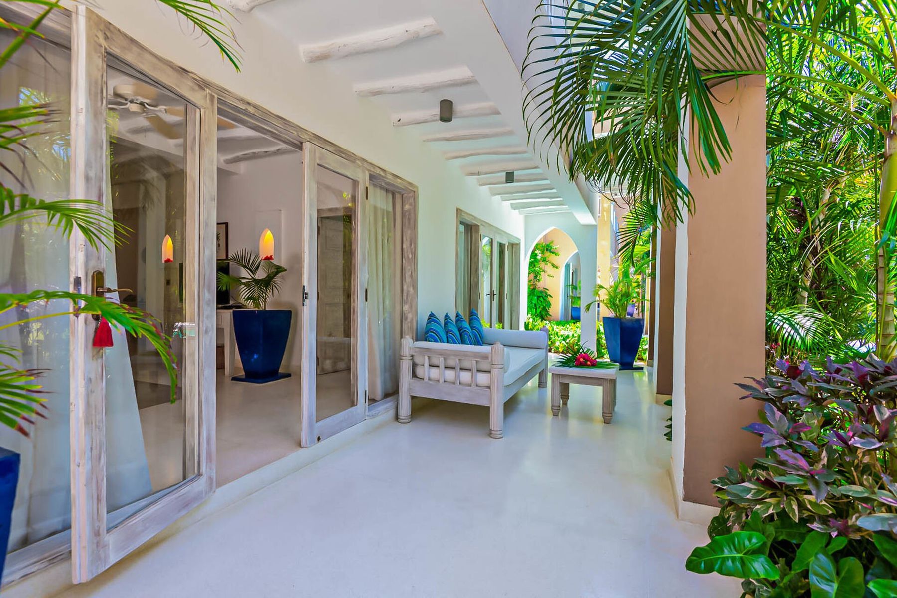 A covered terrace outside an apartment at Medina Palms, with a white bench among tropical plants