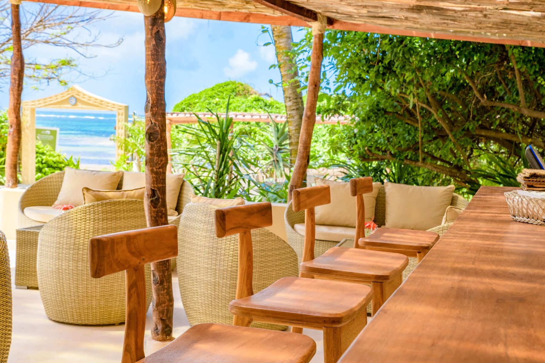 Wicker chairs and a wooden bar under a shady roof at Medina Palms, with the beach and the sea framed beyond