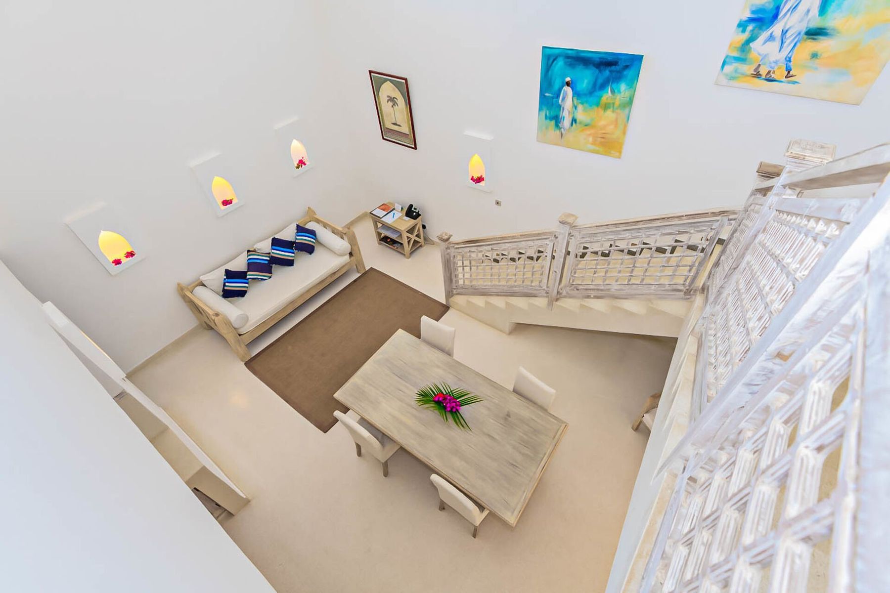 A penthouse living room at Medina Palms seen from the stairs, with a sofa, dining table and carved railings