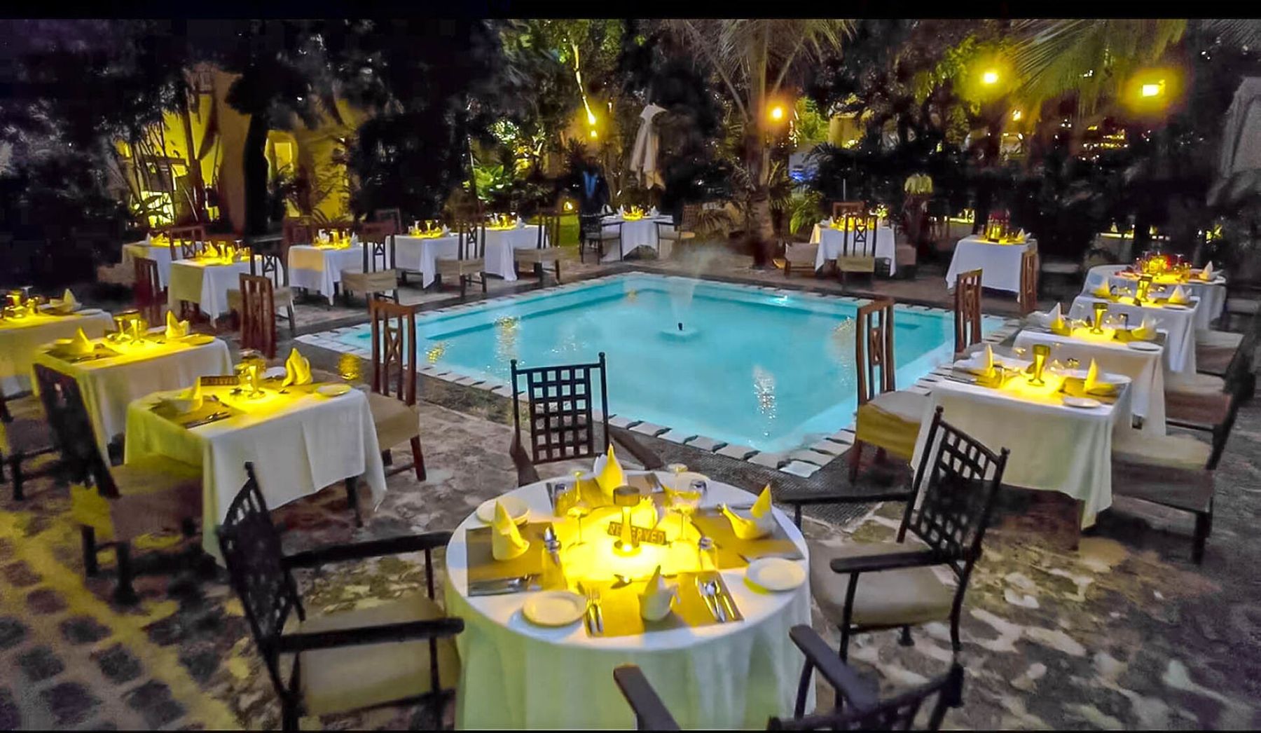 Candlelit tables set around a pool for dinner at Medina Palms in the evening