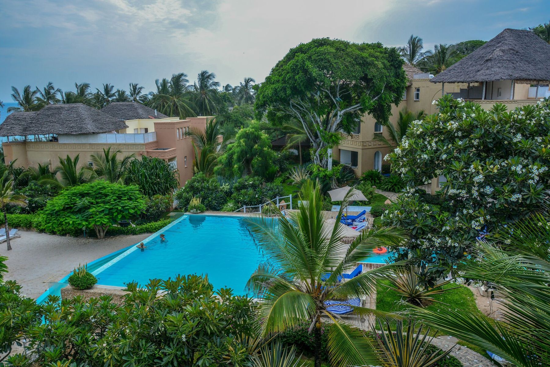 Swahili-style buildings with thatched roofs around a pool and gardens at Medina Palms