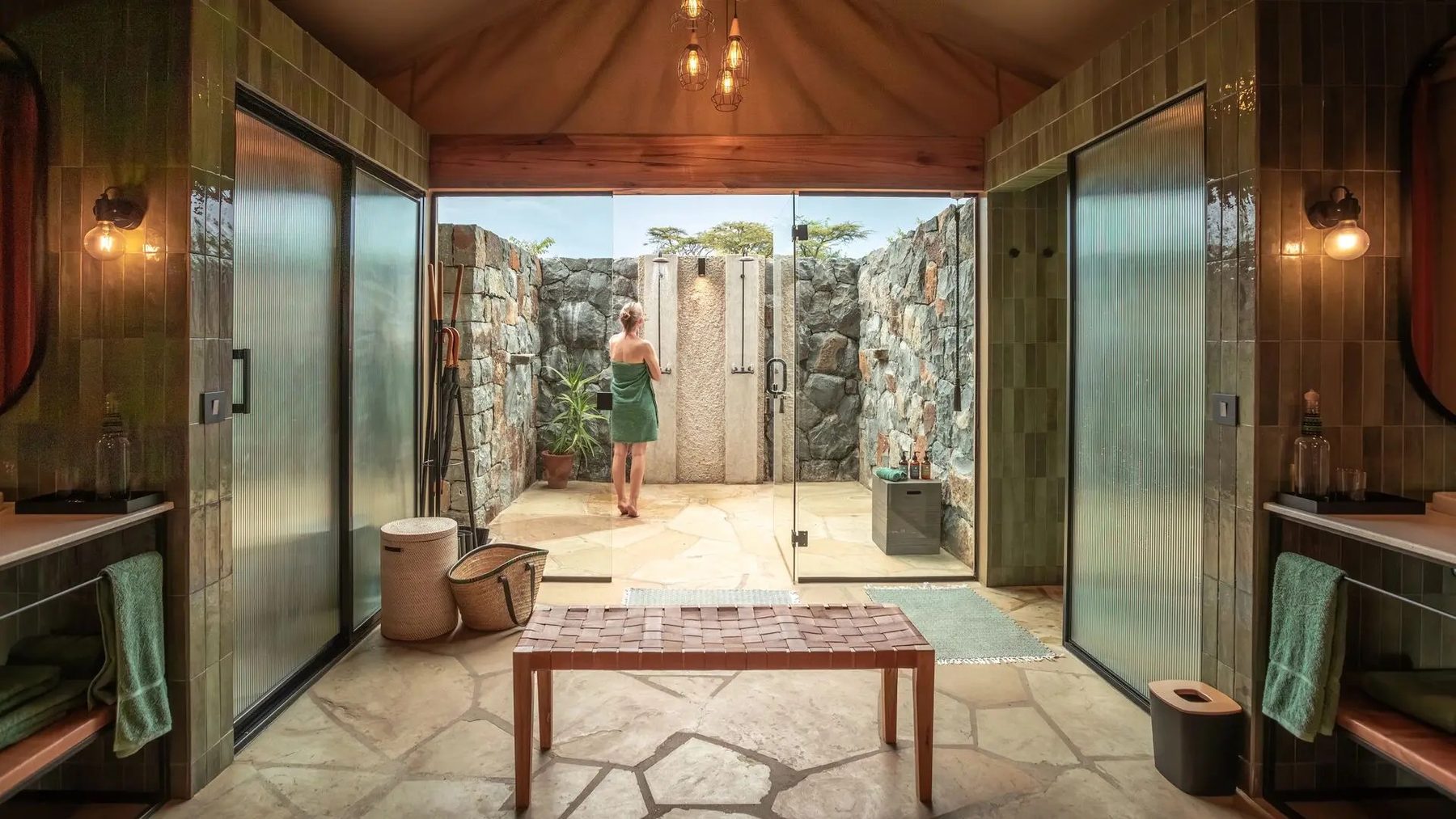 Stone-floored bathroom at Naboisho Camp with twin glass showers and a door opening to an outdoor shower
