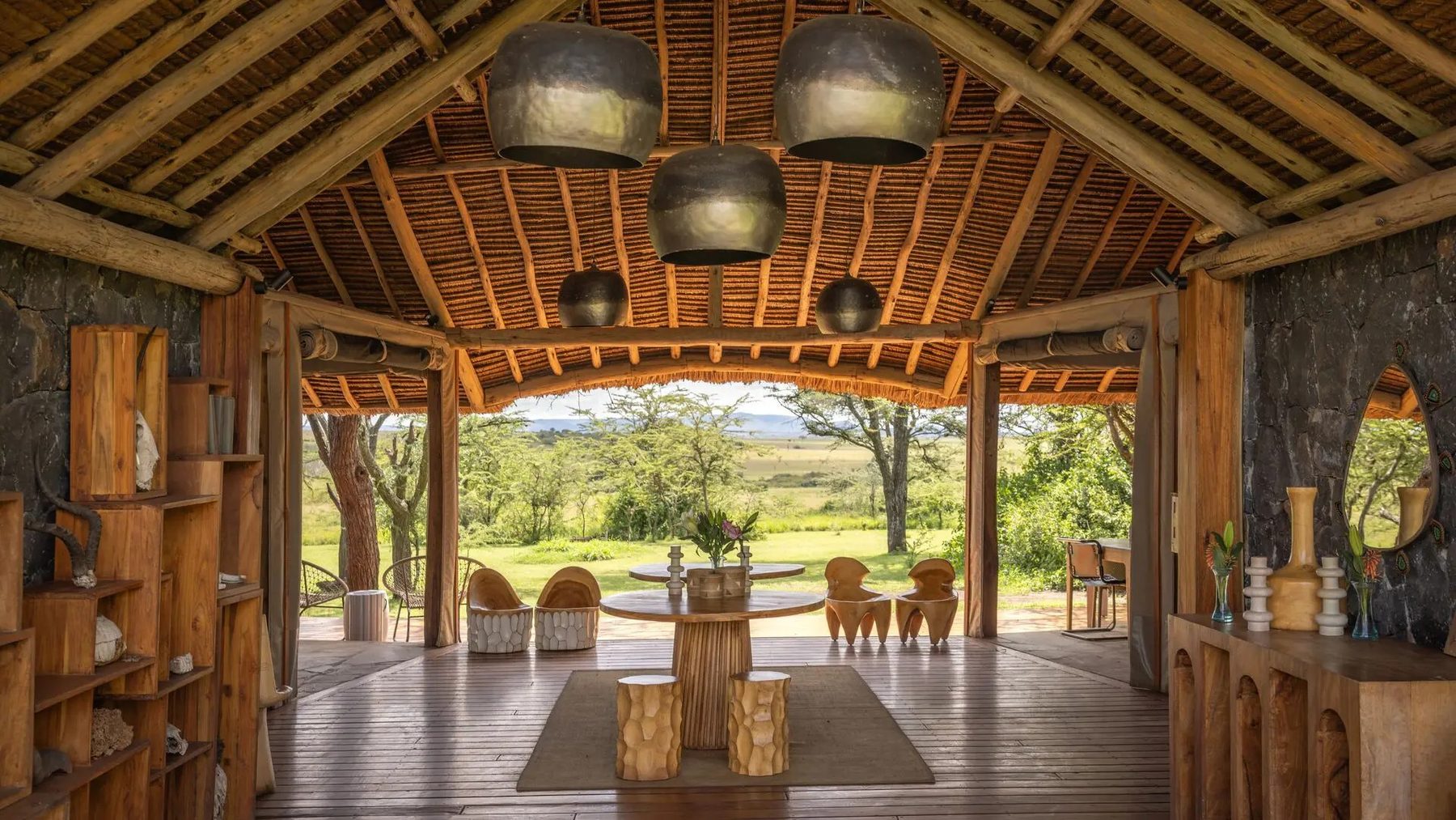 Main area at Naboisho Camp under a high thatched roof with hanging lamps, opening through to a lawn and trees