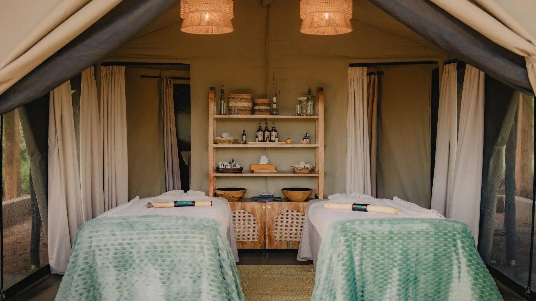 Spa tent at Naboisho Camp with two massage beds under green covers and shelves of oils and baskets