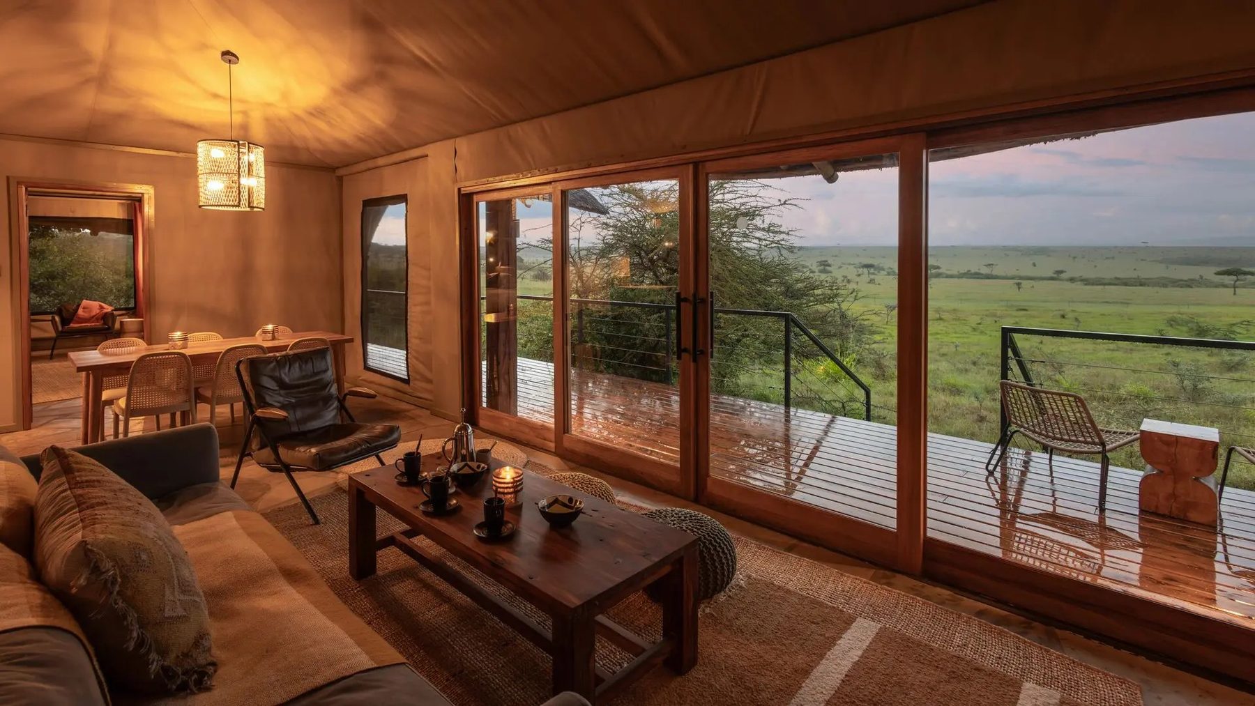 Sitting area inside a tent at Naboisho Camp with a sofa and armchairs, sliding glass doors opening to a deck and plains
