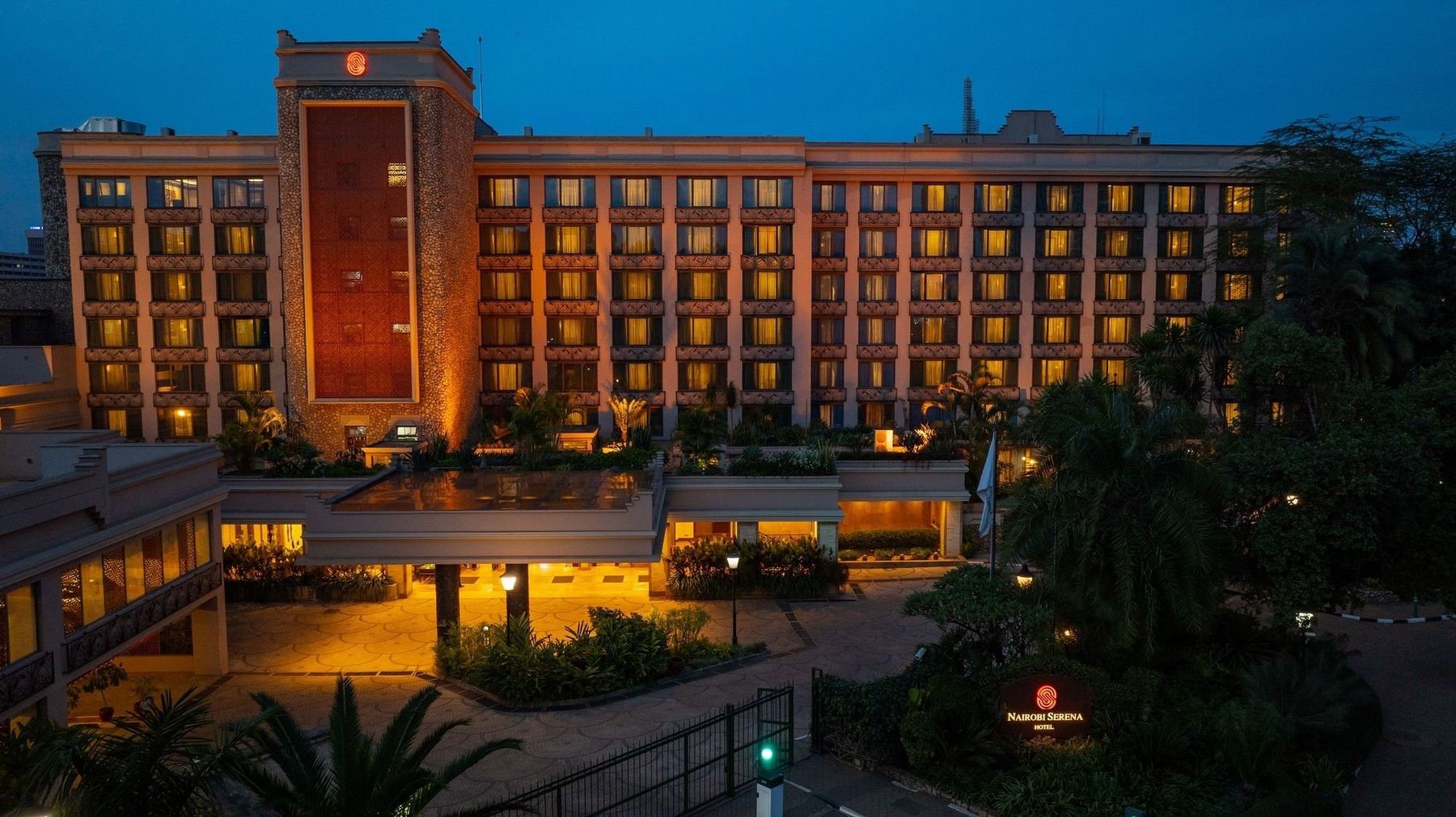 Nairobi Serena Hotel lit up at dusk, with gardens and palms in front of the building