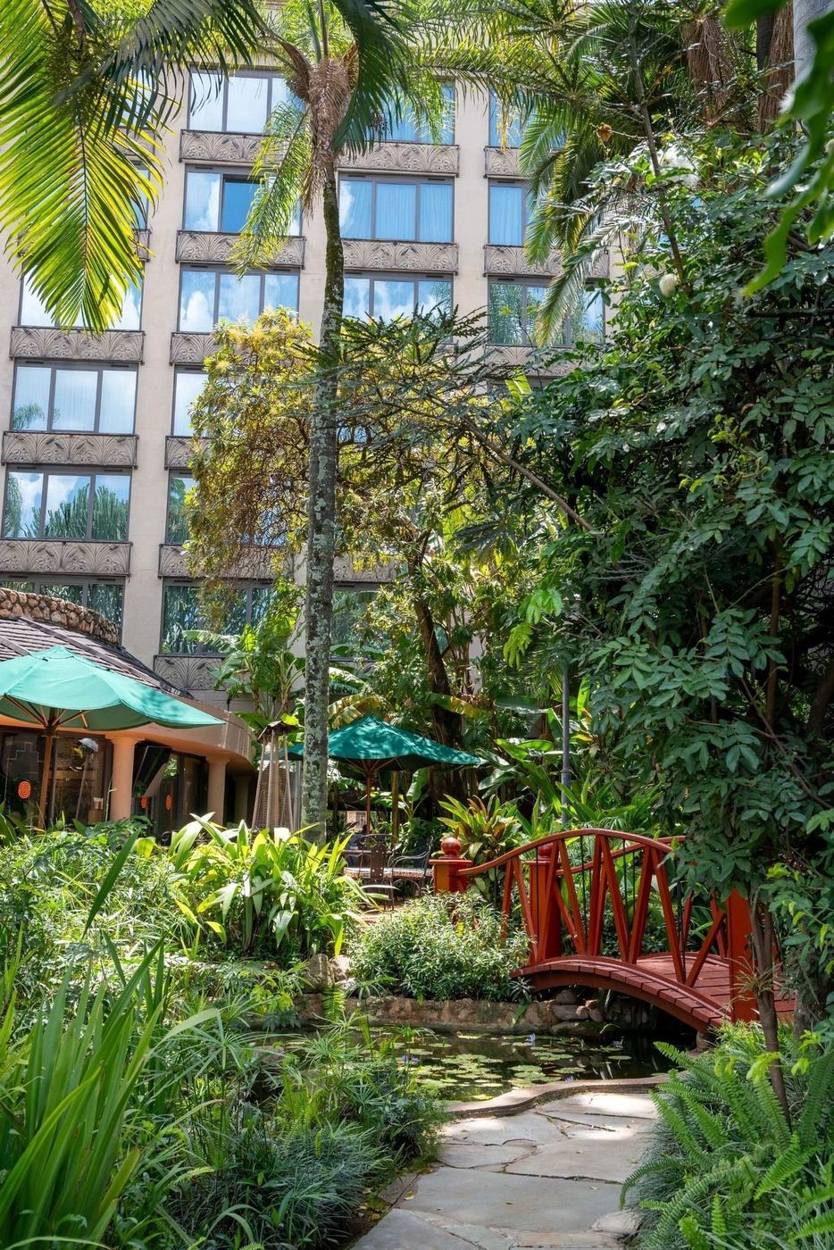 A red wooden footbridge over a lily pond among palms and ferns in the gardens of Nairobi Serena Hotel
