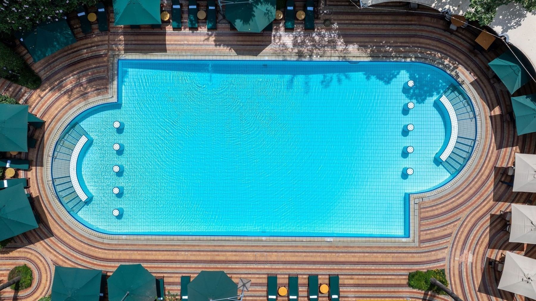 View from above of the pool at Nairobi Serena Hotel, ringed by patterned paving, loungers and green umbrellas