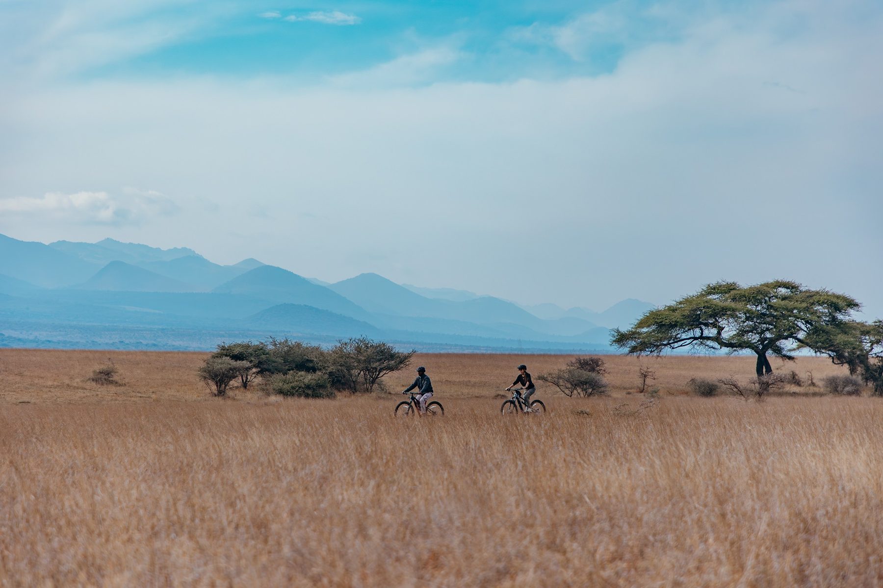 Guests cycling across open grassland near ol Donyo Lodge, with blue hills on the horizon