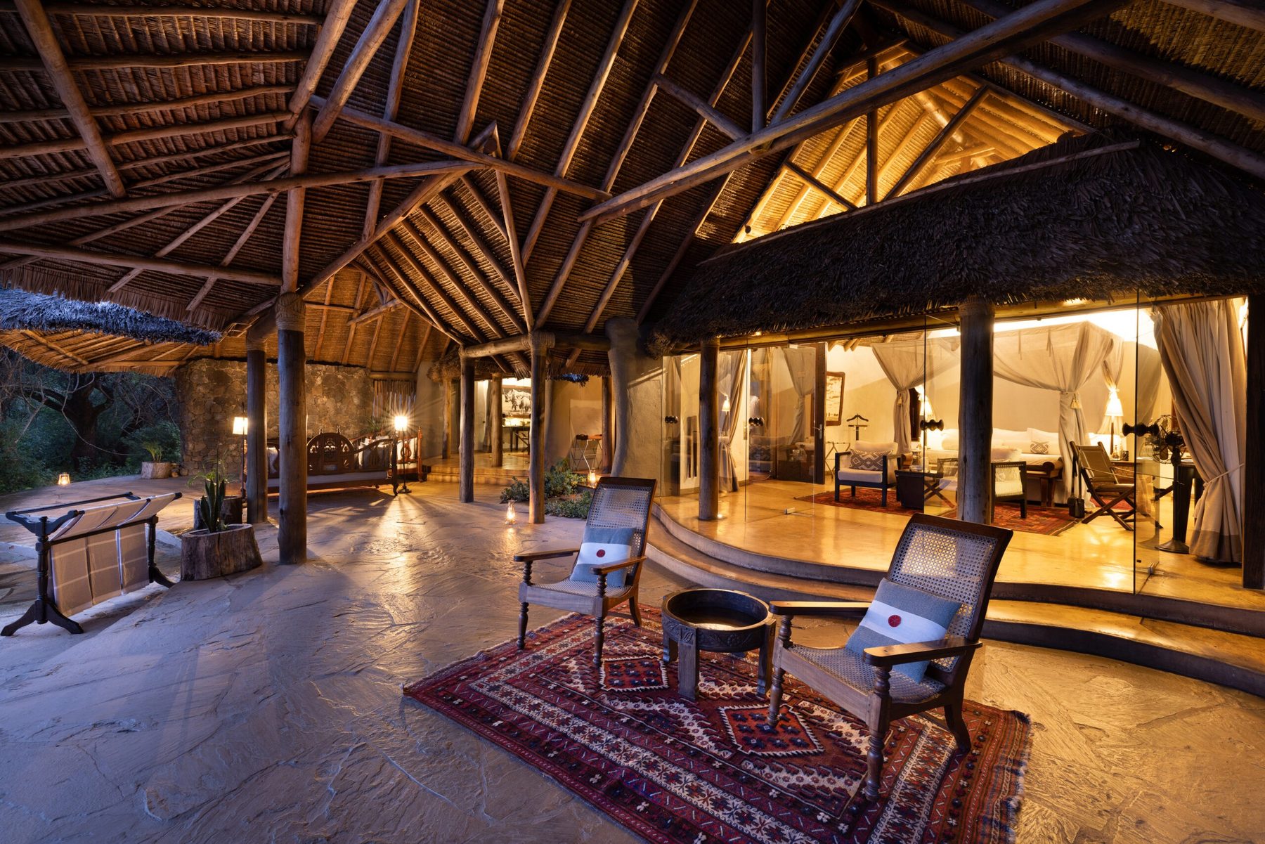 Thatched main lounge at ol Donyo Lodge with armchairs on rugs, lamps and open sides to the bush