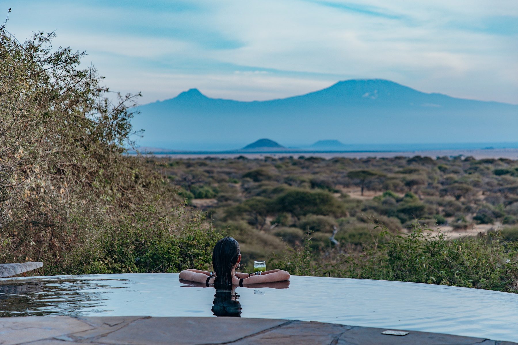 Guest resting at the edge of an infinity pool at ol Donyo Lodge, looking across the bush to Kilimanjaro
