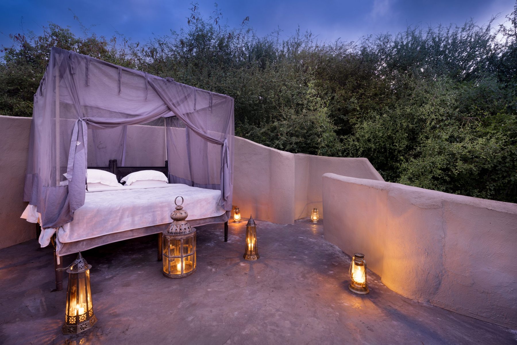 Canopied star bed lit by lanterns on a rooftop terrace at ol Donyo Lodge at dusk