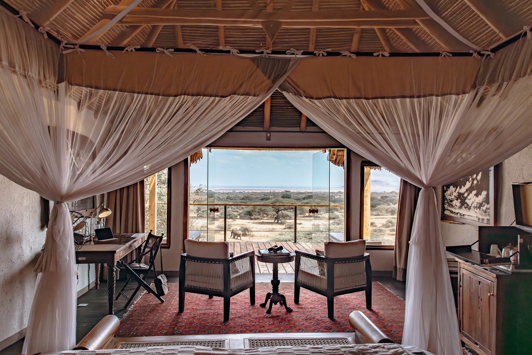 Suite at ol Donyo Lodge seen from the bed, with draped netting, armchairs and glass doors onto a deck and the plains