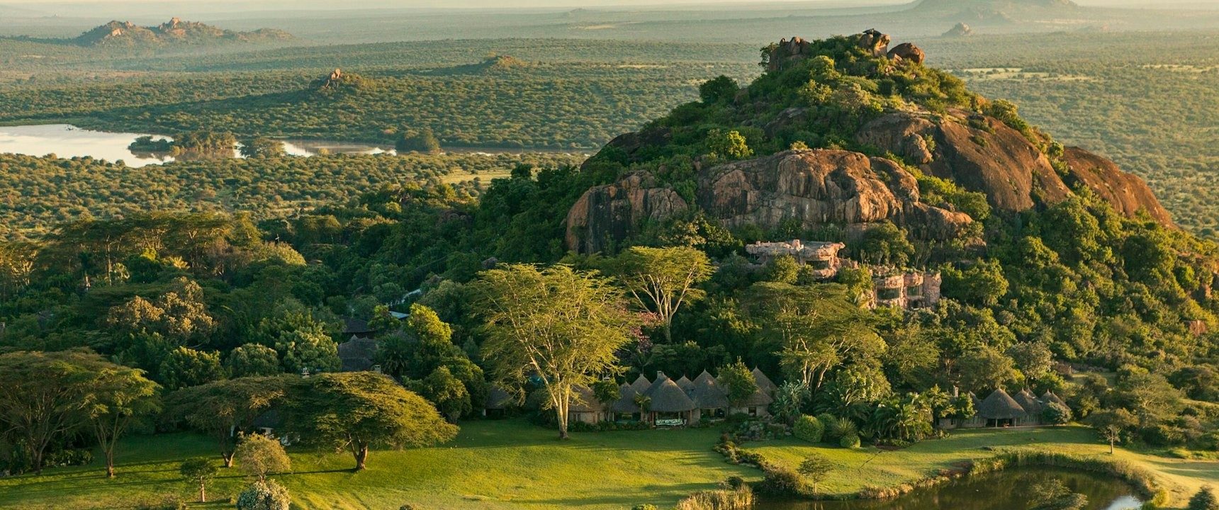 Aerial view of a rocky kopje rising from green bush and lawns at Ol Jogi, plains stretching beyond