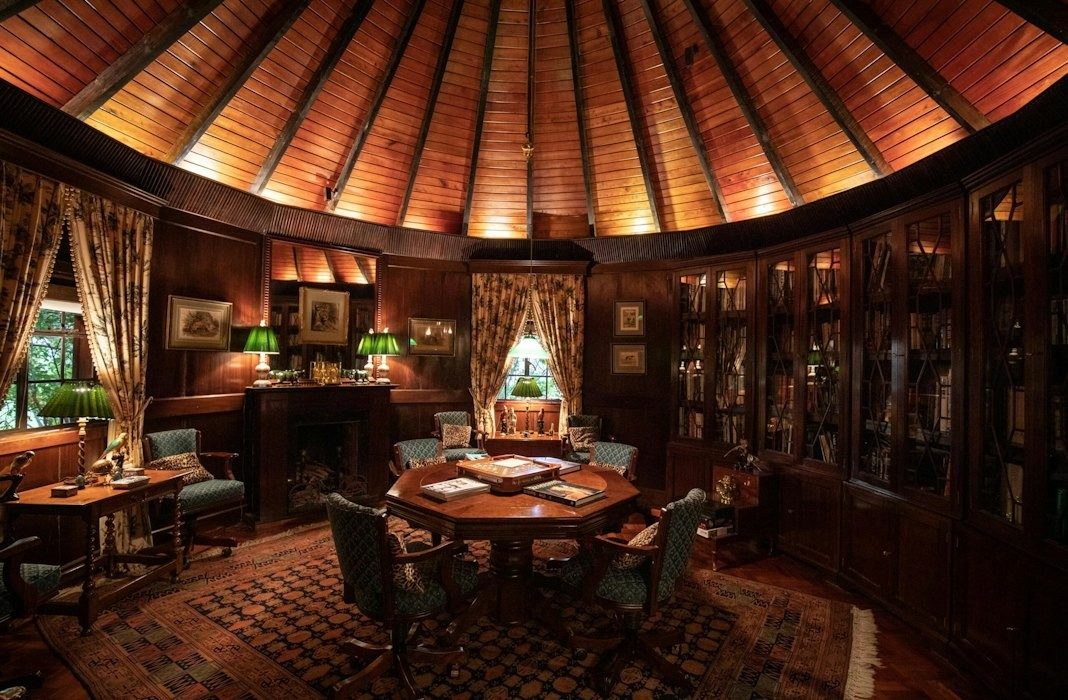 Round wood-panelled library at Ol Jogi with bookcases, a card table and green lamps under a radiating ceiling