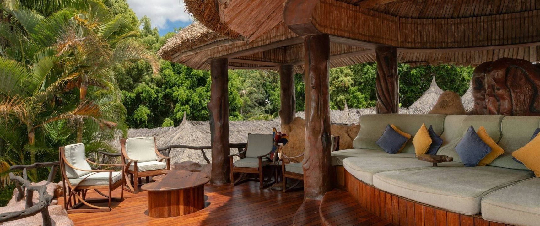 Open thatched lounge at Ol Jogi with a long curved sofa, blue cushions and carved wooden pillars