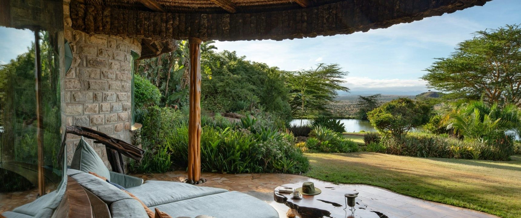 Shaded veranda with sofas at Ol Jogi looking over a green lawn and gardens to distant hills