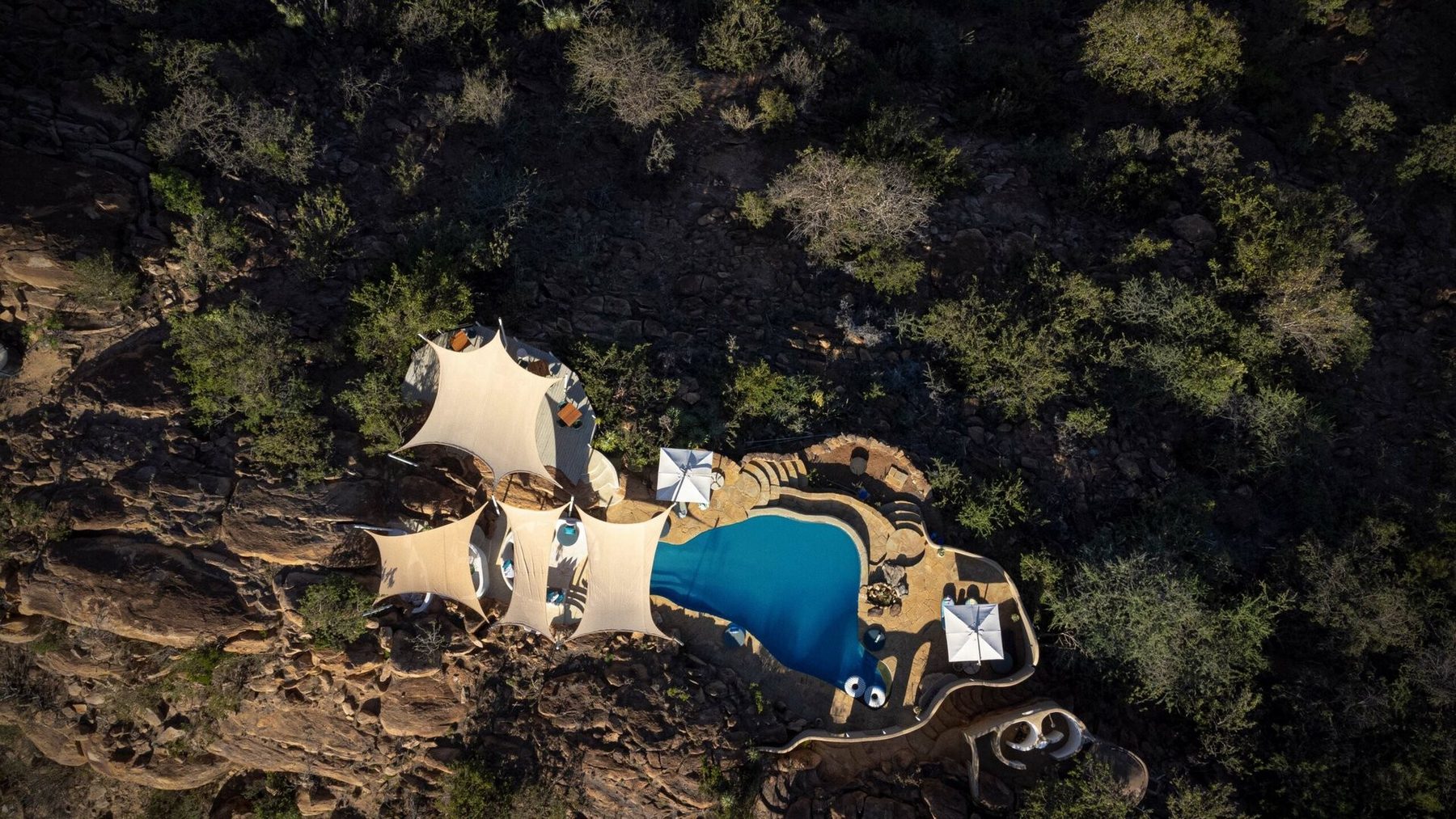 Aerial view of Ol Lentille’s pool and white shade sails tucked among rocks and dense bush
