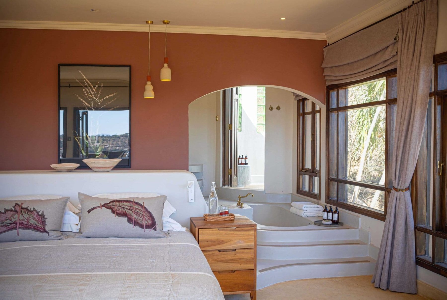 Bedroom at Ol Lentille with terracotta walls, a sunken bath and tall windows looking out over the bush