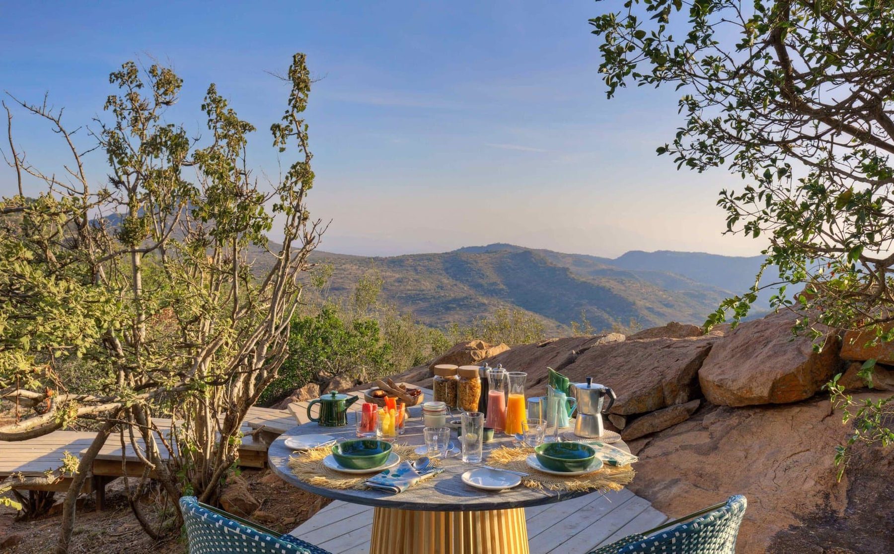 Breakfast table laid on the rocks with a view across bush-covered hills at Ol Lentille