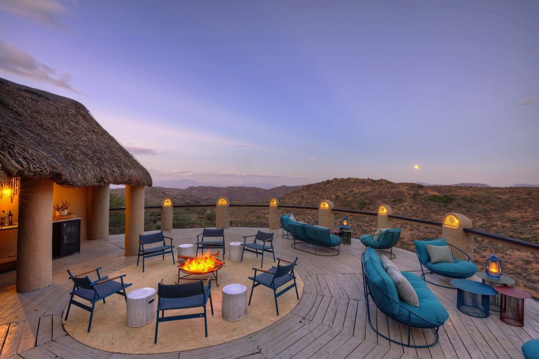 Circle of blue chairs around a fire on a stone terrace at Ol Lentille, with hills fading into the dusk
