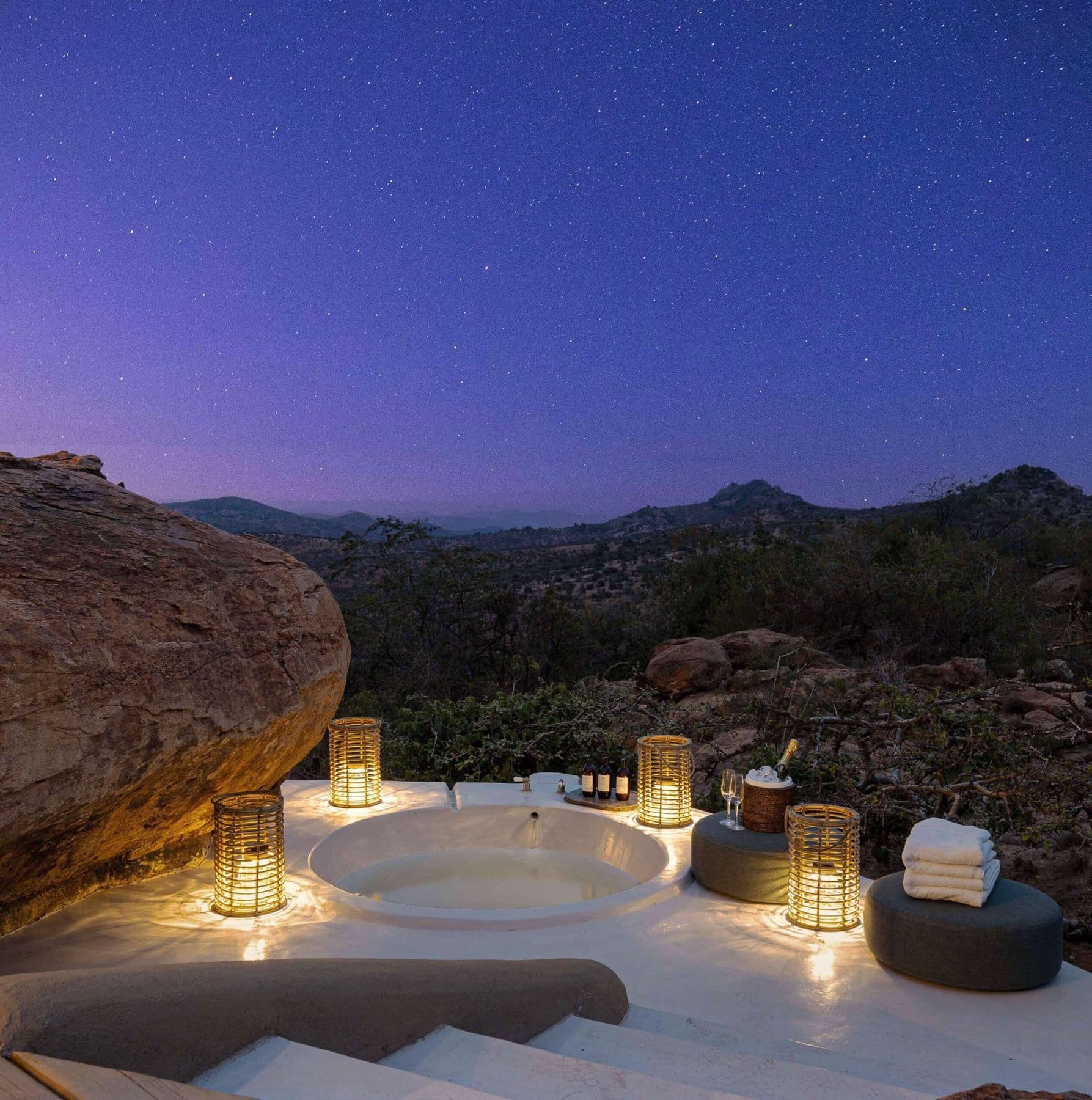 Candlelit outdoor bathtub set among boulders at Ol Lentille, with hills under a starry evening sky