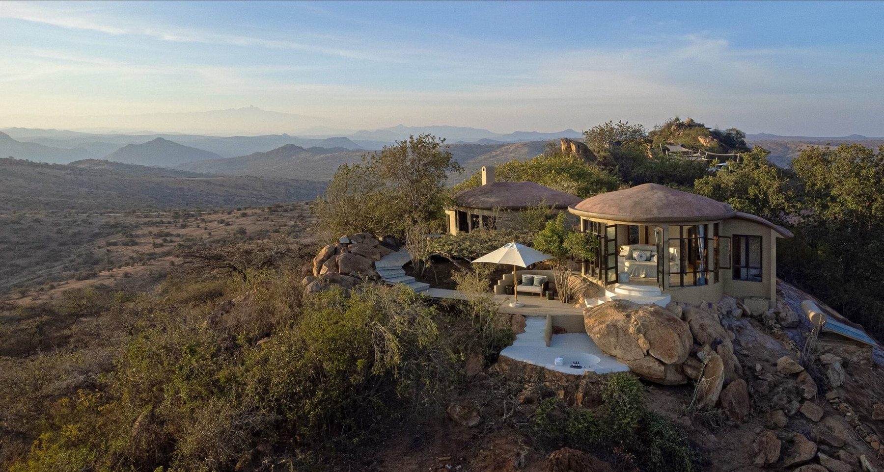 Thatched villa at Ol Lentille perched on a rocky outcrop above a wide valley of bush and hills