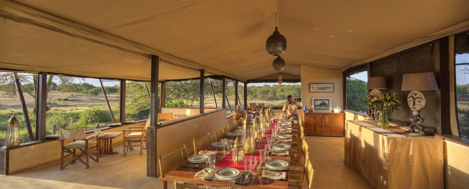 Long dining table laid for a meal under canvas at Ol Pejeta Bush Camp, with views out over the bush