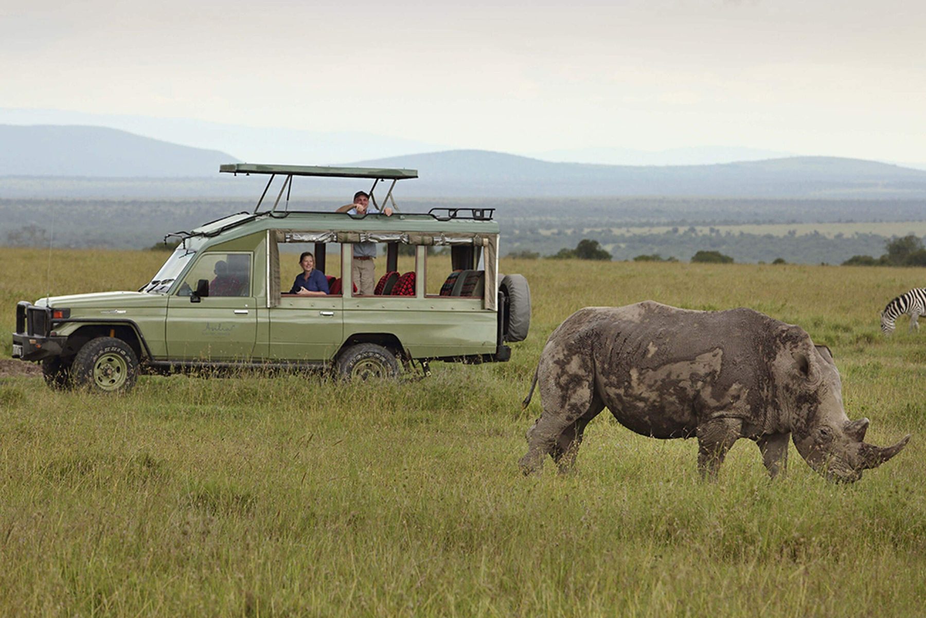 Guests in a game drive vehicle watching a rhino graze on open grassland near Ol Pejeta Bush Camp