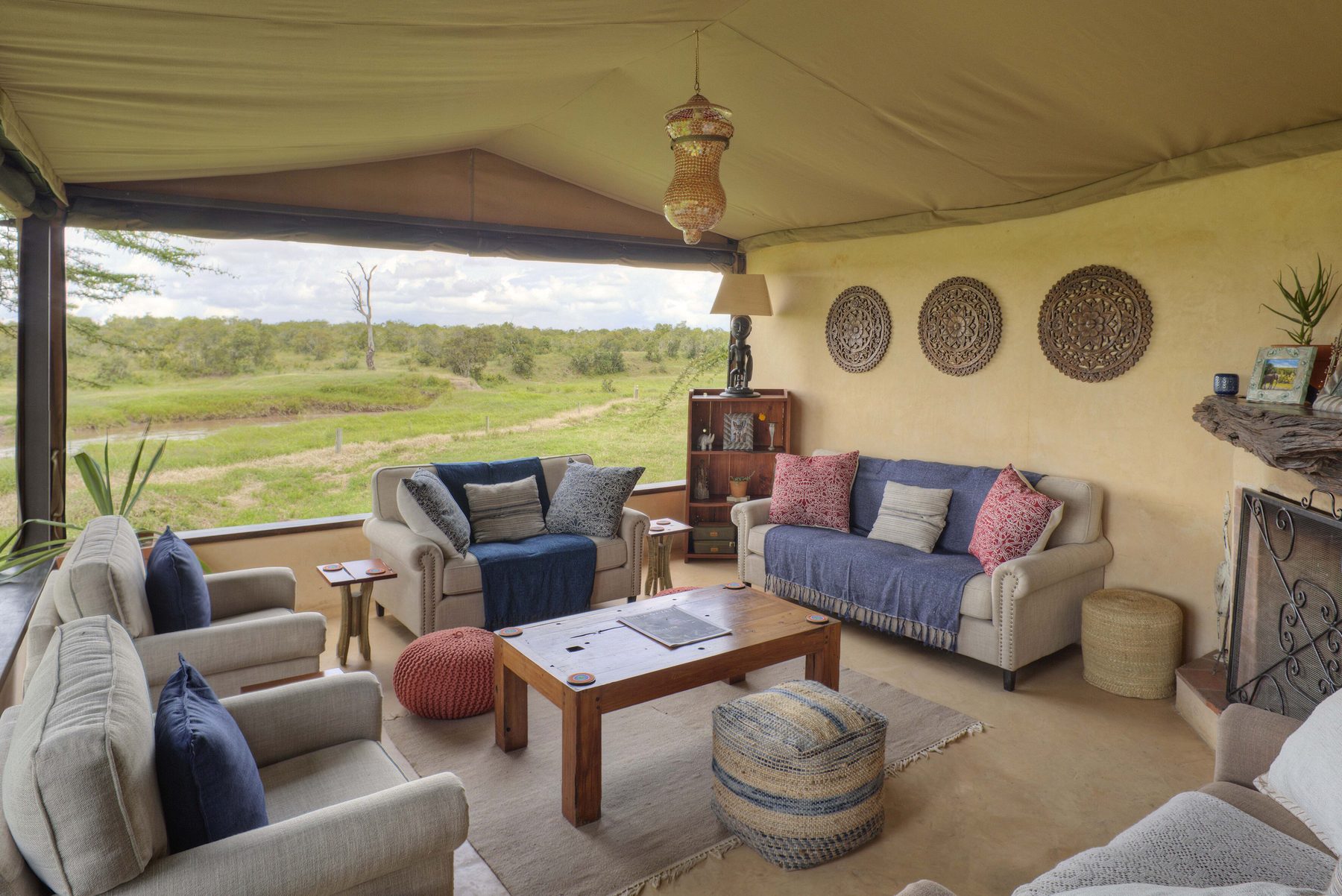 Lounge tent at Ol Pejeta Bush Camp with blue and grey sofas, woven wall baskets and open sides onto green plains