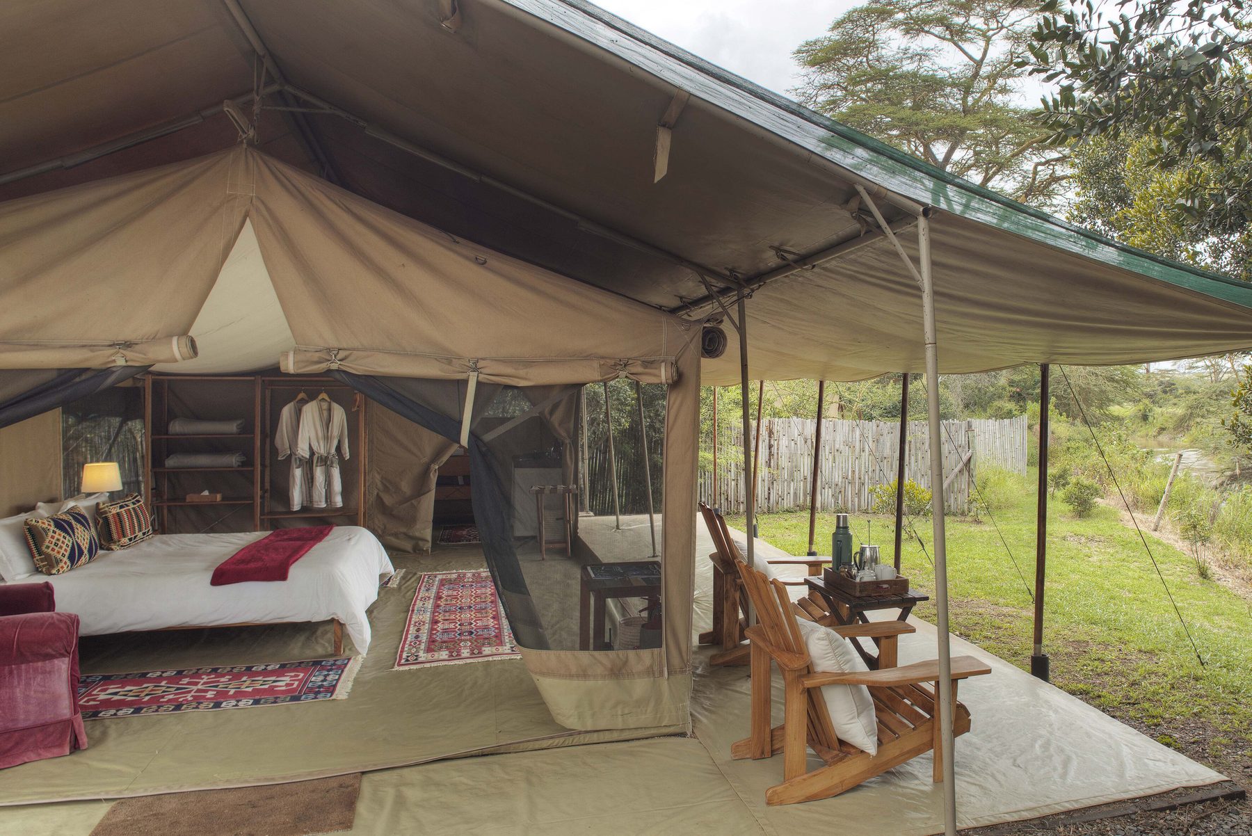 Tent at Ol Pejeta Bush Camp with its front open to a veranda with wooden deck chairs facing the grassland