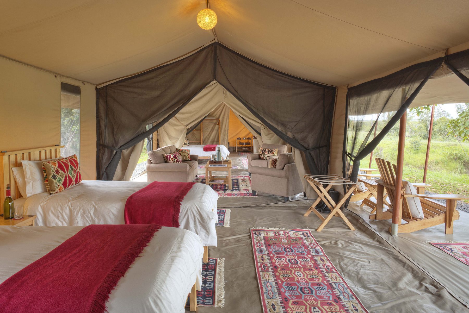 Twin tent at Ol Pejeta Bush Camp with red throws on white beds, woven rugs and a lantern hanging from the canvas