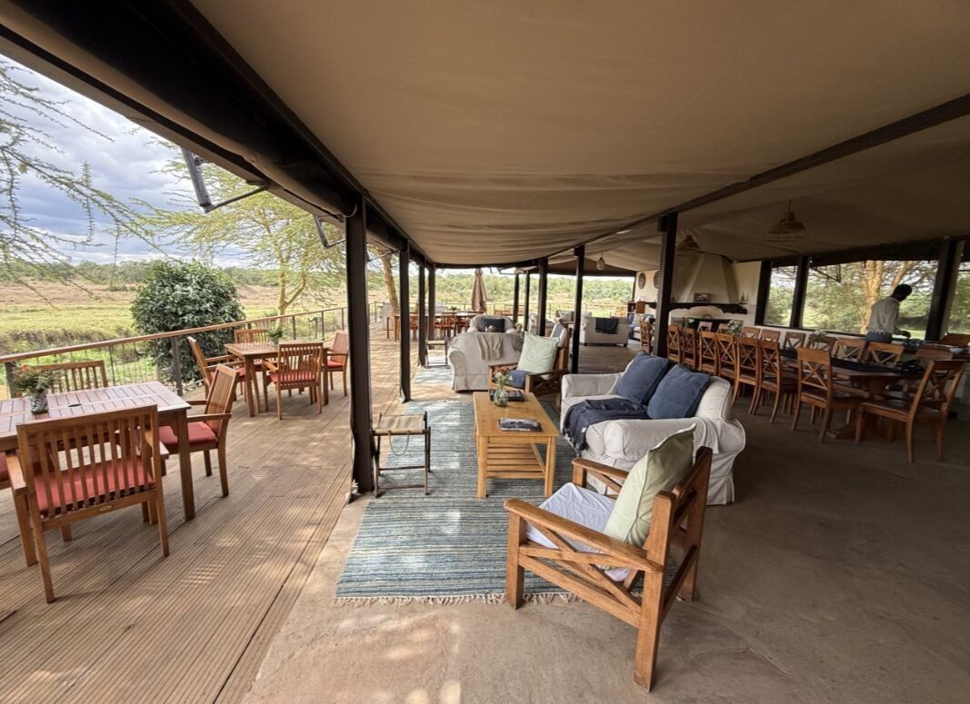 Covered wooden veranda at Ol Pejeta Bush Camp with cushioned chairs and tables looking out over the grassland