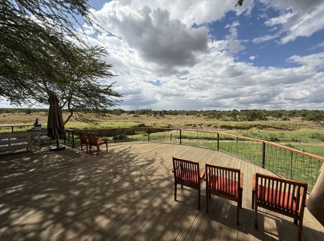 Shaded viewing deck with red chairs behind a railing at Ol Pejeta Bush Camp, looking over green plains