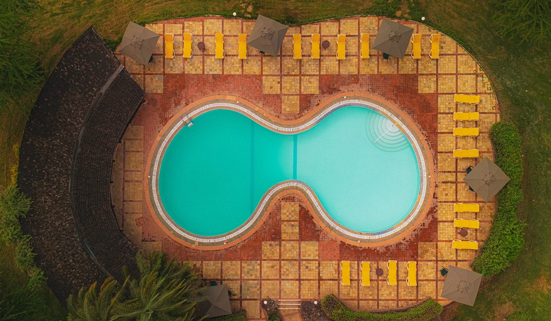 Overhead view of the figure-eight swimming pool and its brick terrace with loungers at Ol Tukai Lodge
