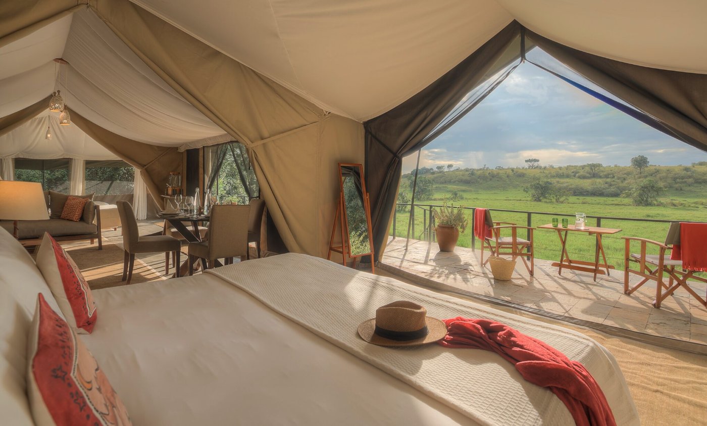 Tent interior with a bed and dining table, opening onto a deck facing green plains at Kicheche Mara North