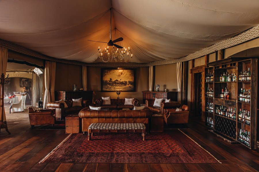 Tented lounge with leather sofas, a chandelier and a bar cabinet at Mara Plains Camp