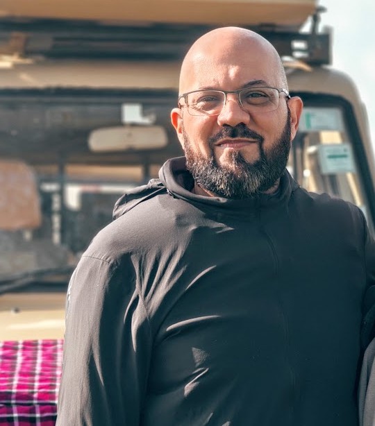 Shafiq Jagani, Director and Lead Safari Consultant, smiling in front of a safari vehicle
