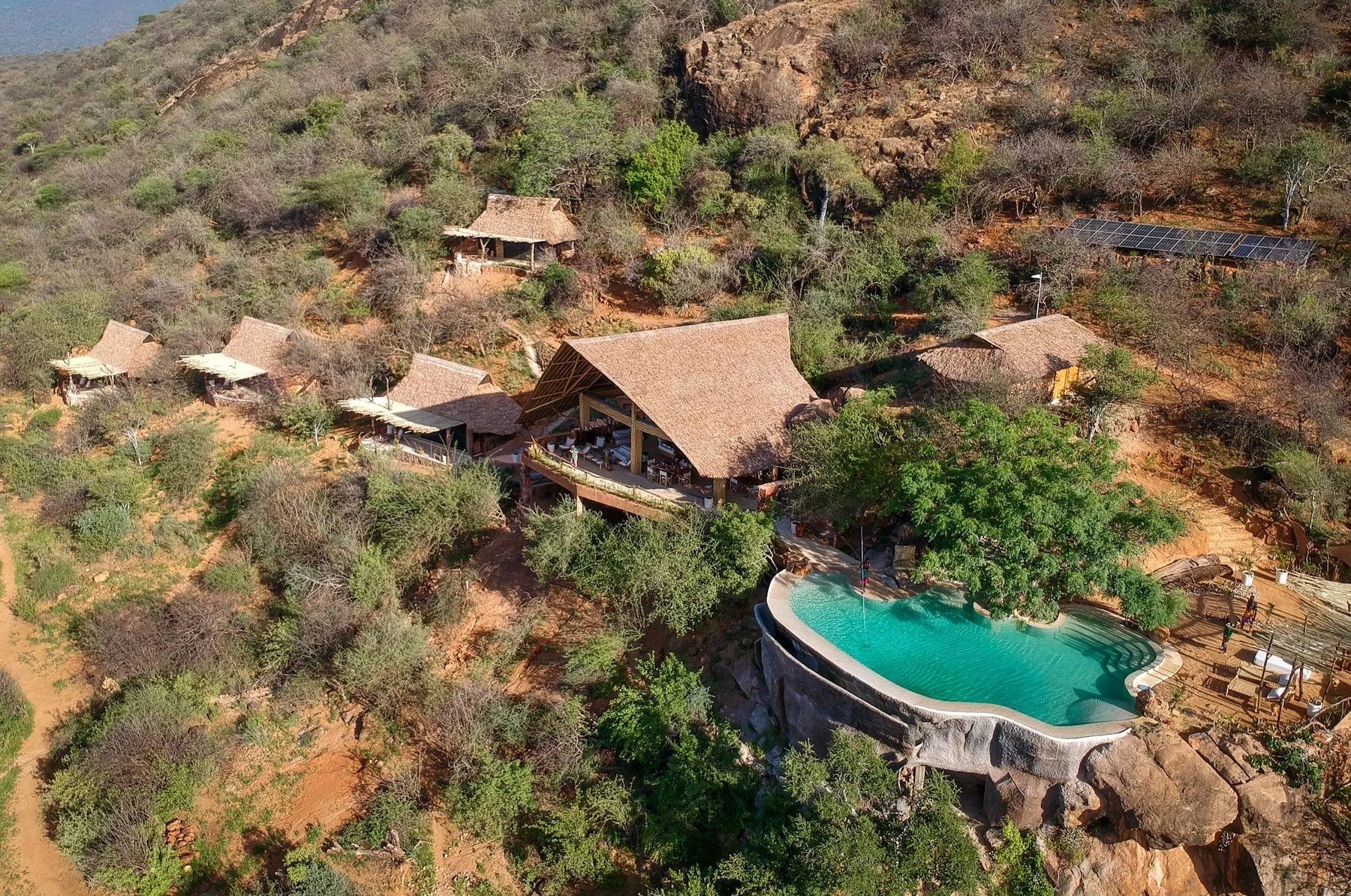 Aerial view of the thatched buildings and curved pool of Reteti House among rocks and green bush