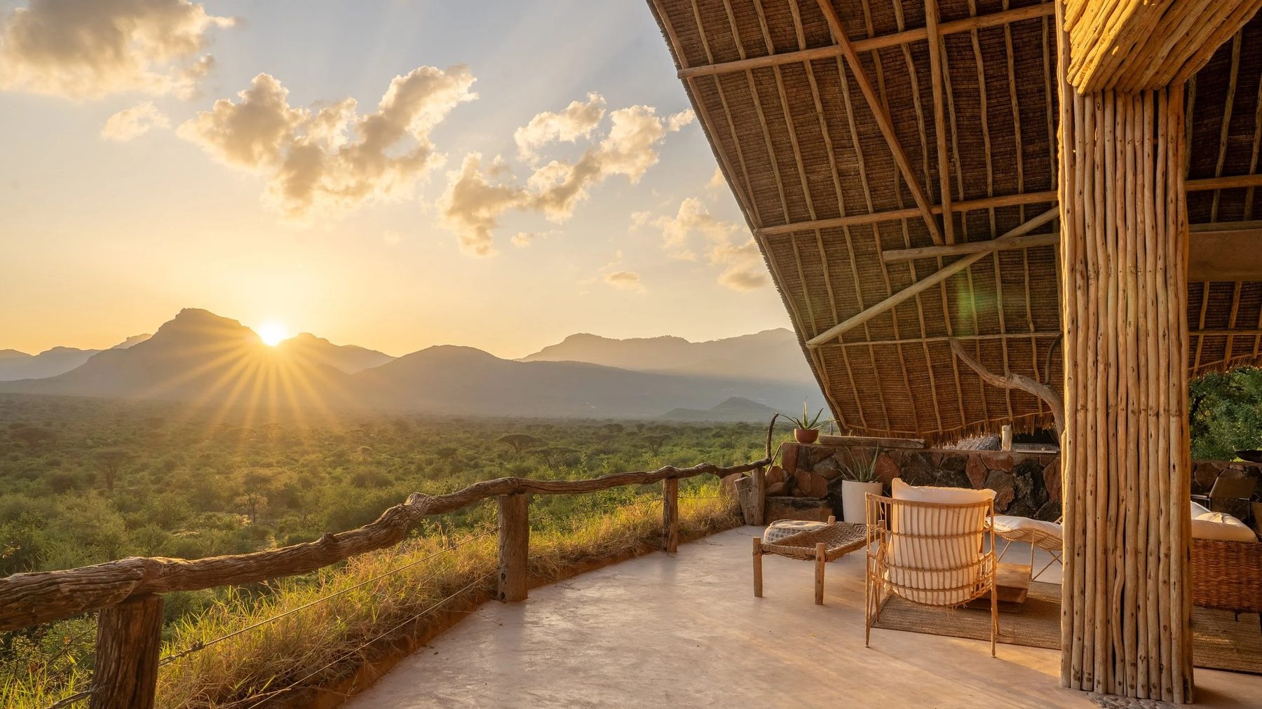 Sun setting over the hills beyond a thatched deck with chairs at Reteti House