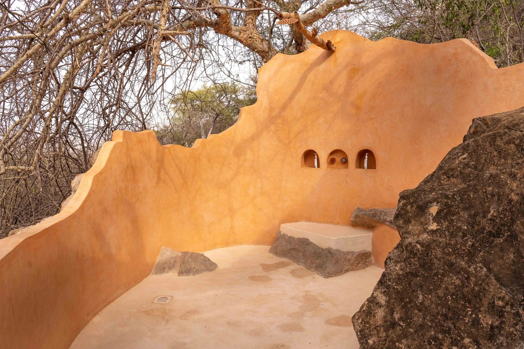 Open-air shower at Reteti House with curved ochre walls, carved niches and a branch for a shower head