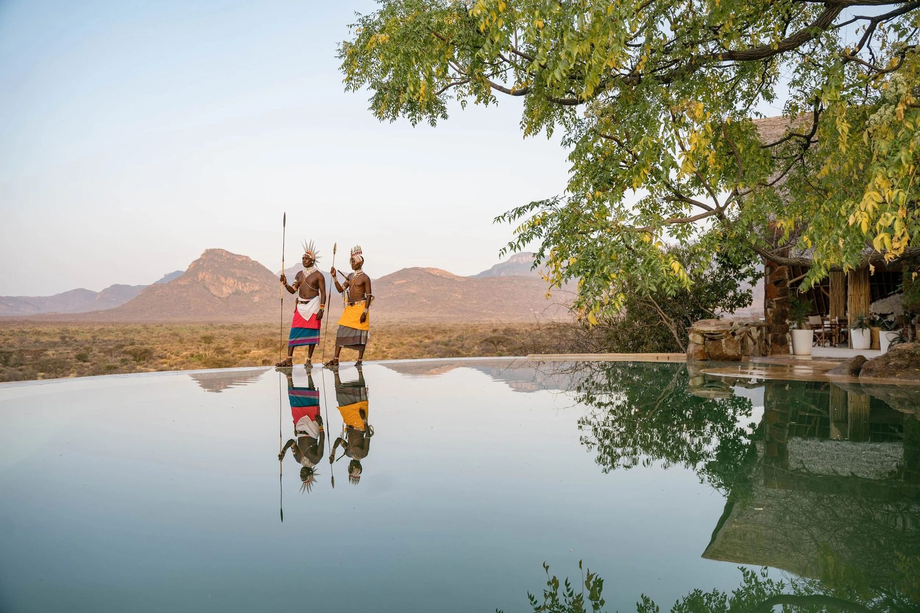 Two Samburu warriors reflected in the still infinity pool at Reteti House, with mountains beyond