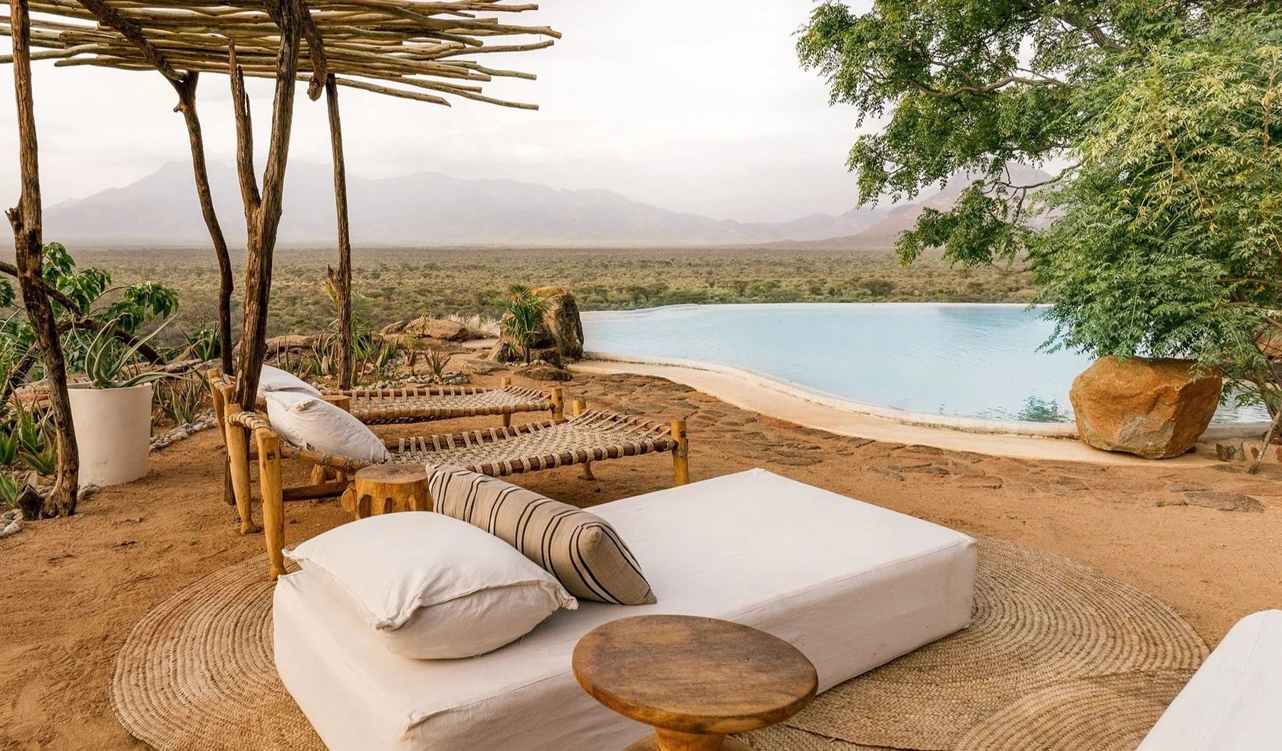 Cushioned daybeds under thatch on a sandy terrace beside the pool at Reteti House