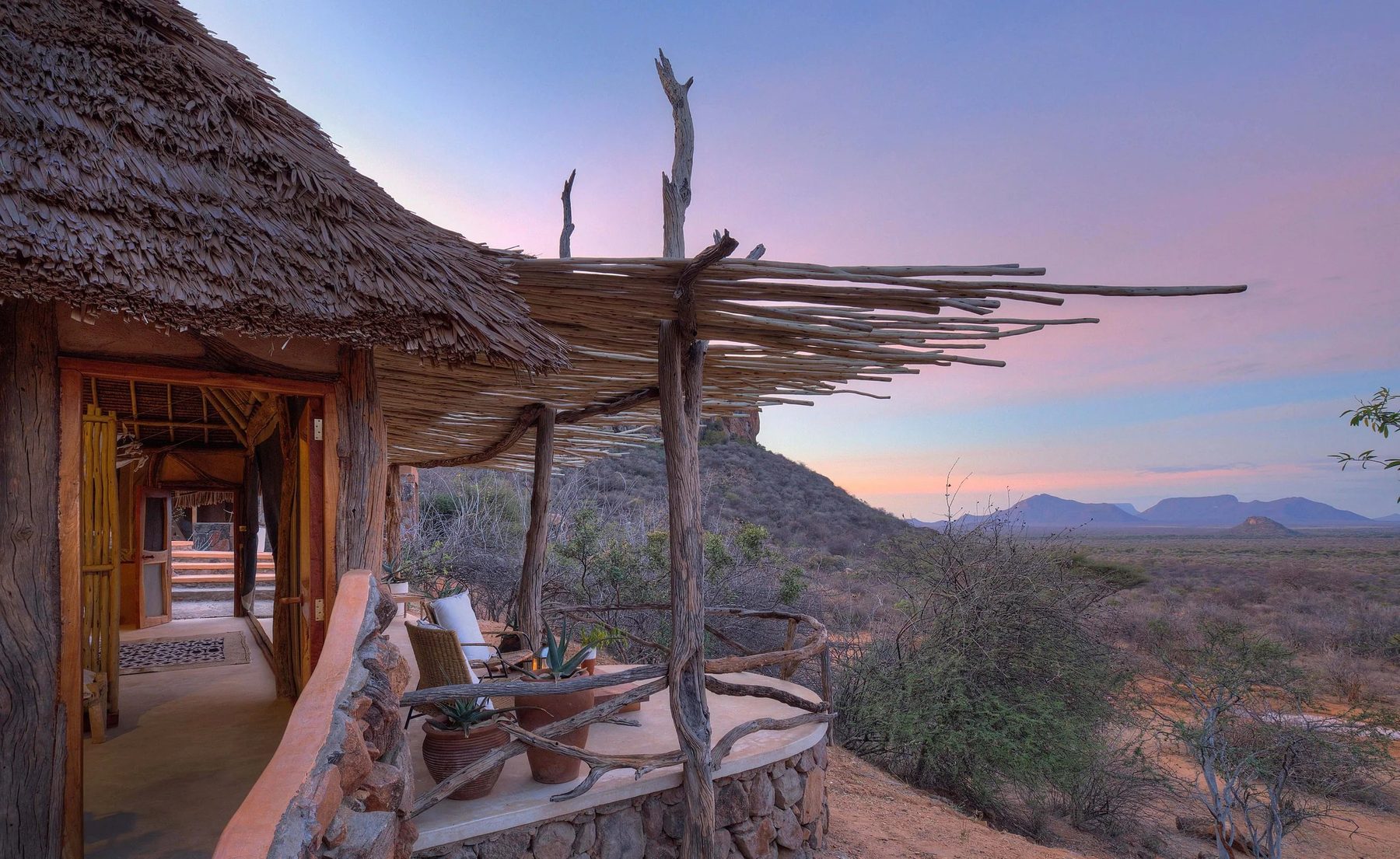 Thatched walkway and veranda with seating at Reteti House at dusk, with hills on the horizon