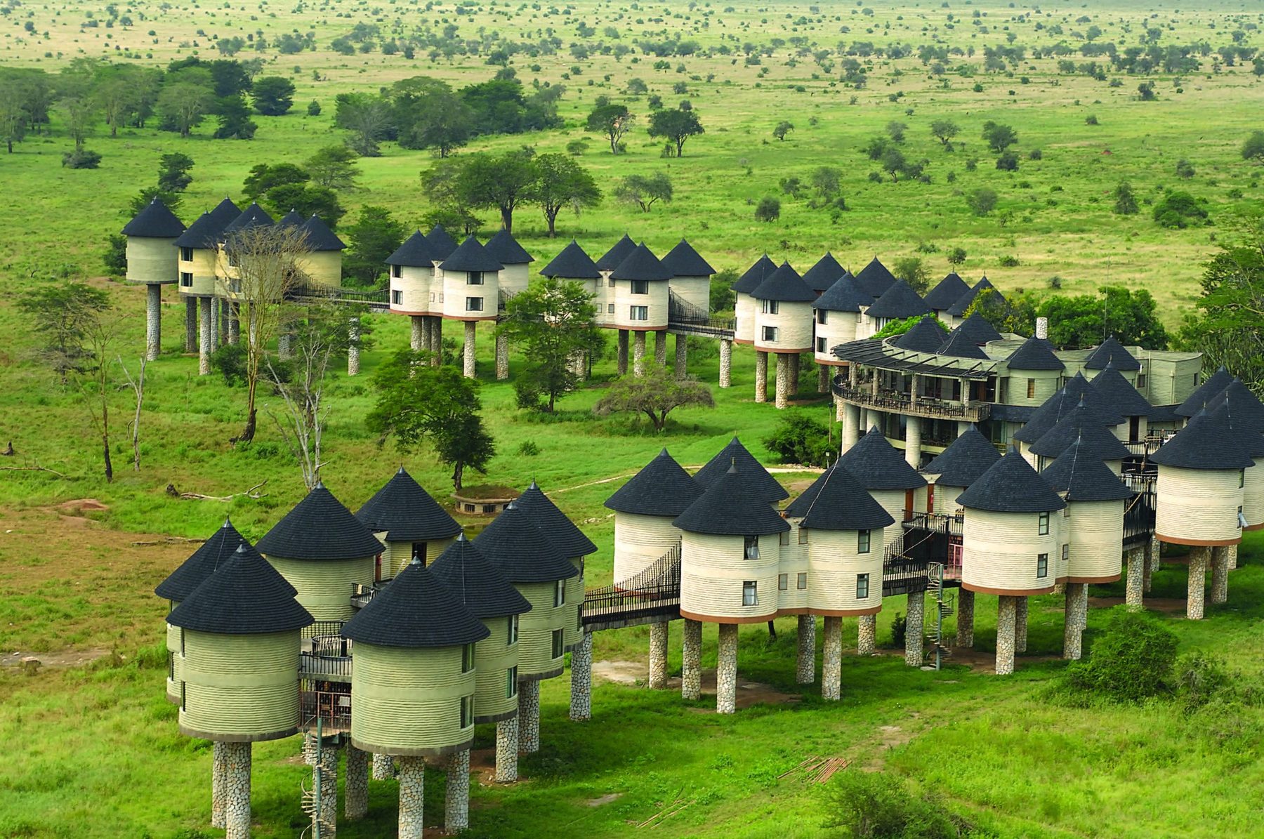Aerial view of Salt Lick Safari Lodge’s rows of stilted thatched rooms on green grassland dotted with trees
