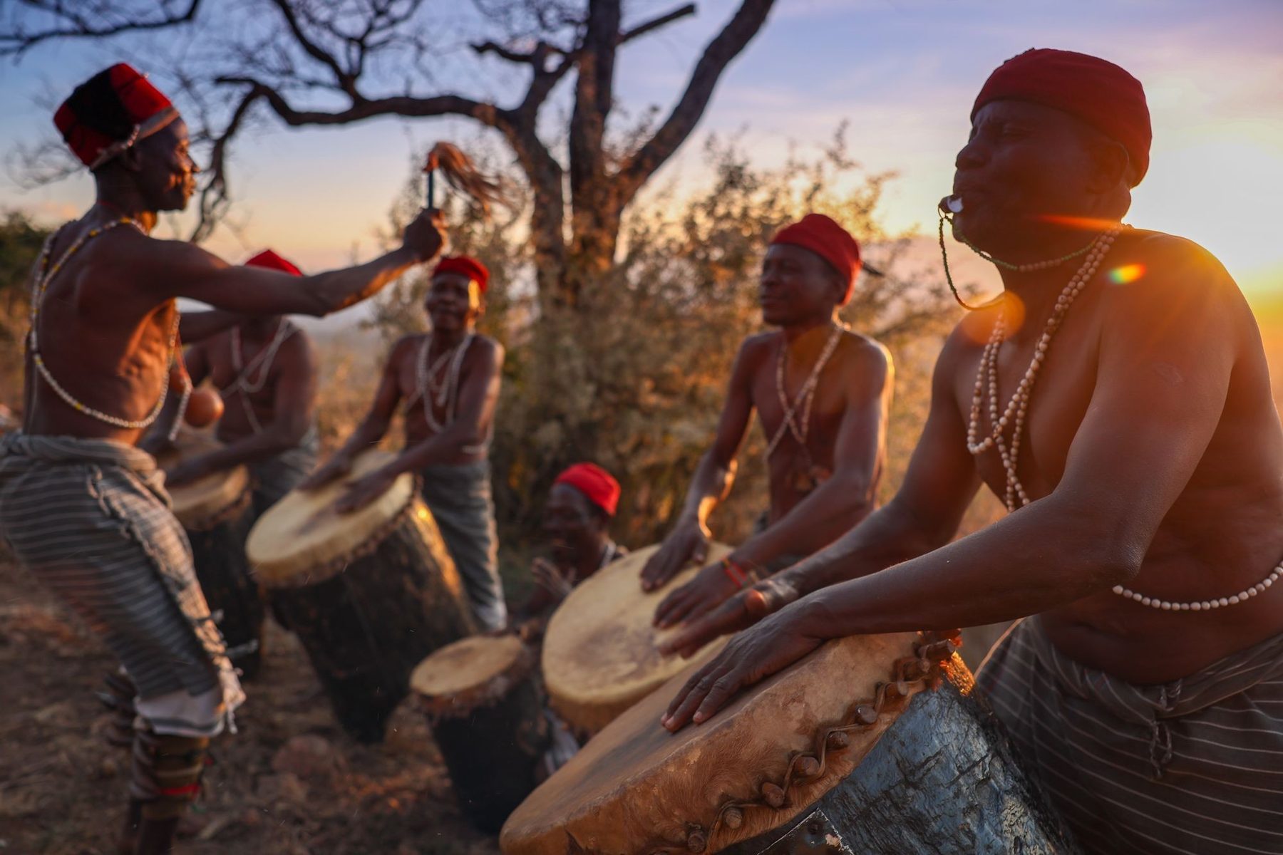 Drummers and dancers performing with large hand drums in warm evening light