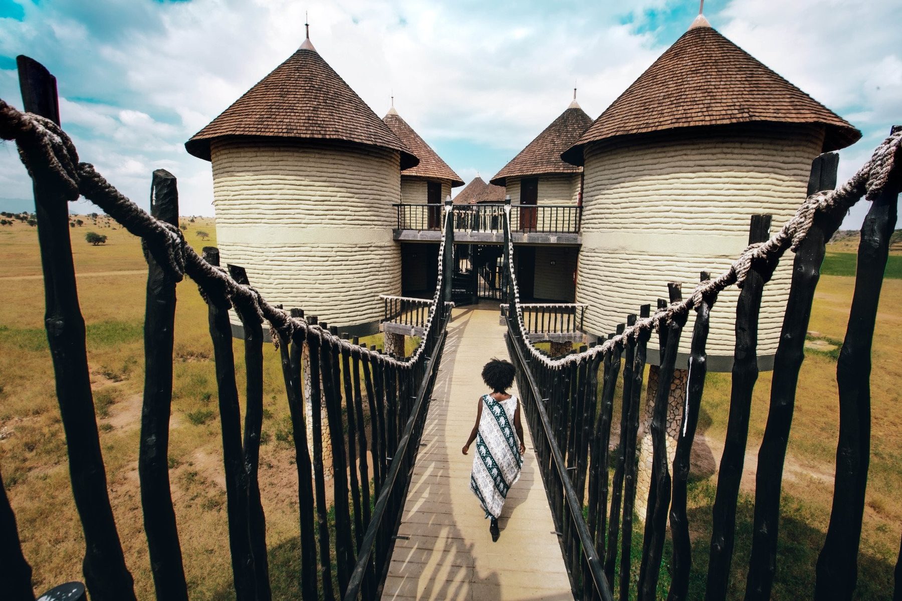 Guest crossing a rope bridge walkway towards round thatched rooms on stilts at Salt Lick Safari Lodge